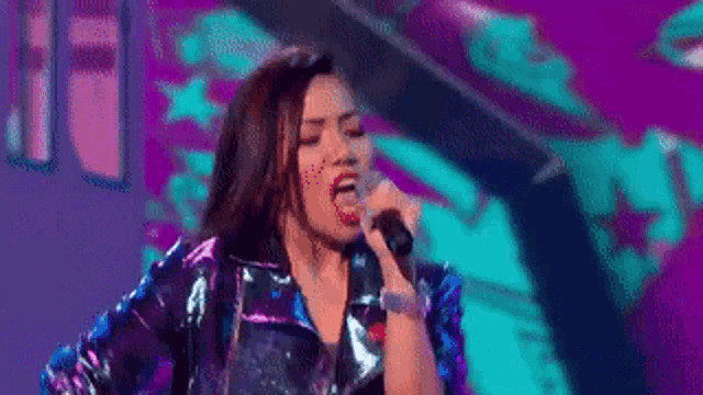 a woman in a blue jacket is singing into a microphone on a stage .
