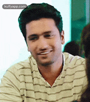 a man in a striped shirt is smiling and looking at the camera while sitting at a table .