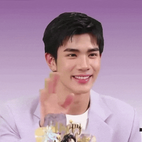 a young man in a purple suit is smiling and making a peace sign .