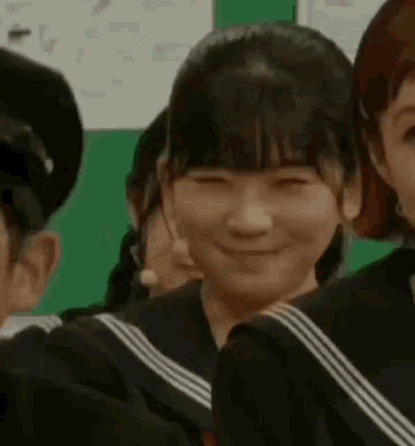 a girl in a school uniform is smiling in front of a group of girls .