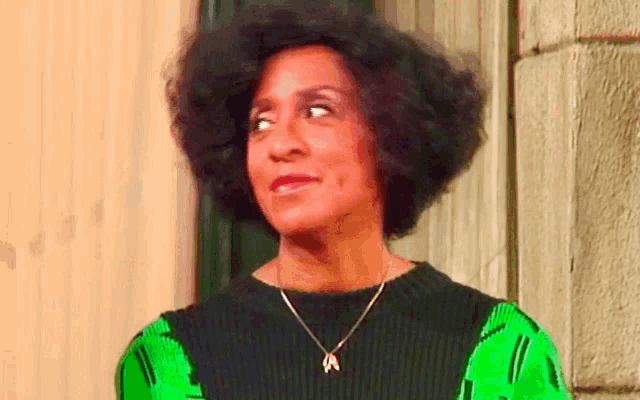 a woman wearing a green and black sweater and a gold necklace
