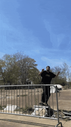 a man is standing on a skateboard behind a fence wearing a black t-shirt that says supreme