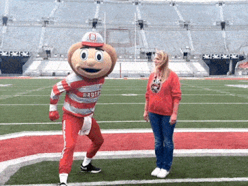 a woman stands on a football field with a mascot that says buckeyes