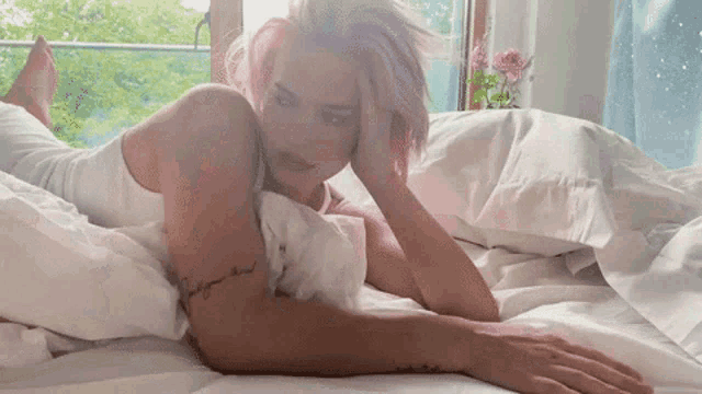 a woman with pink hair is laying on a bed