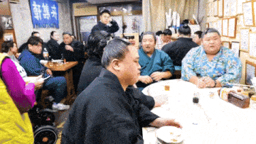 a group of people are sitting around a table in front of a sign that says ' kyoshin ' on it