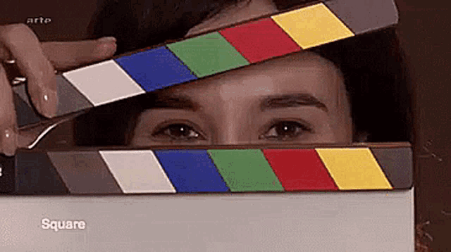 a woman is holding a clapper board over her face and the word square is on the box