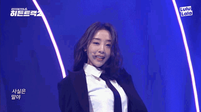 a woman in a suit and tie is dancing on a stage with lulu lala written on the bottom