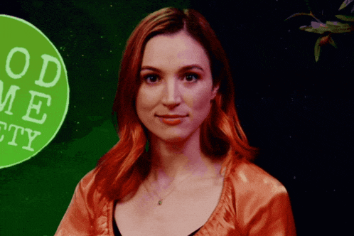 a woman with red hair stands in front of a green sign that says good me pretty