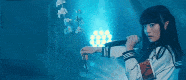 a girl in a school uniform is holding a microphone and a flower in her hand .
