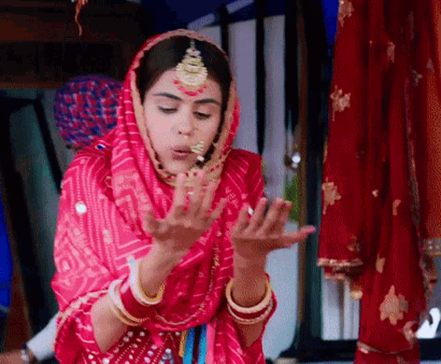 a woman in a red dress with a veil on her head is holding something in her hands .