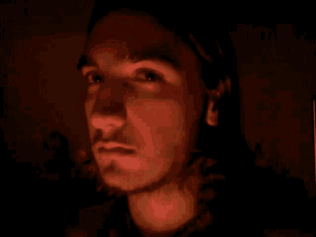 a man with long hair and a beard looks at the camera in the dark