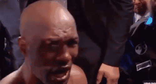 a bald man is crying in a boxing ring while a man in a suit stands behind him .