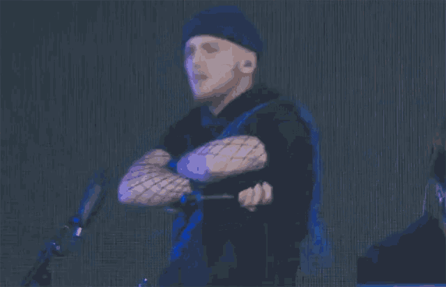 a man wearing fishnet gloves stands in front of a microphone with his arms crossed