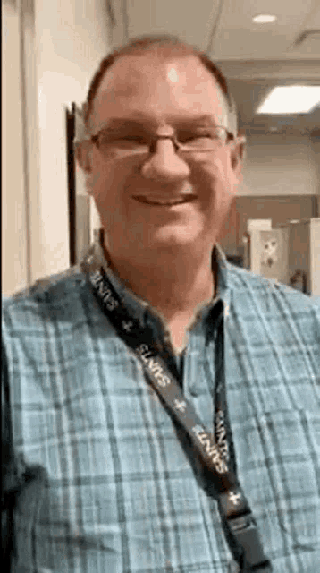 a man with glasses and a lanyard around his neck is smiling .