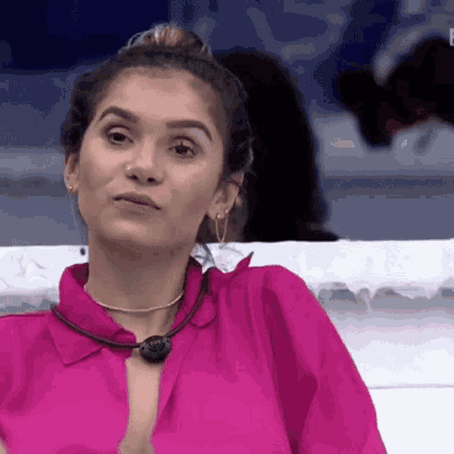 a woman wearing a pink shirt and earrings is sitting in front of a white wall .