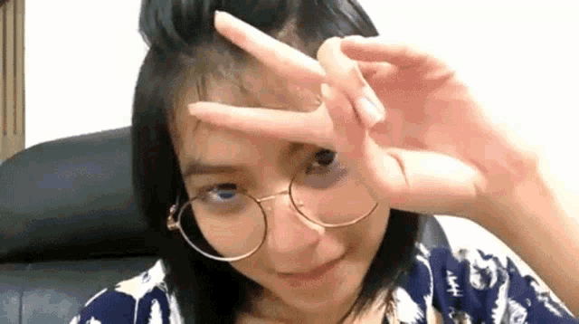 a young woman wearing glasses is making a peace sign with her hand .