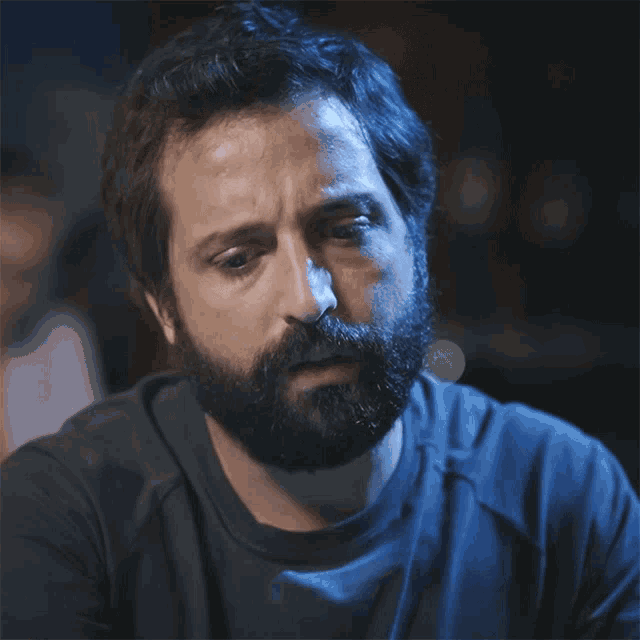 a man with a beard is wearing a blue shirt and making a surprised face