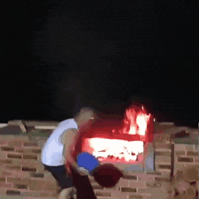 a man throws a bucket of water into a fire pit at night
