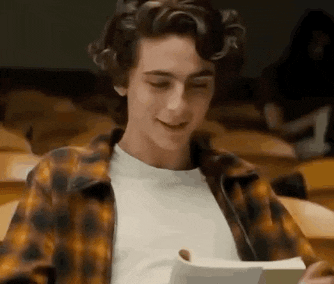 a young man in a plaid shirt is sitting in a lecture hall reading a book .