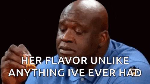 a bald man in a blue shirt is eating a chicken nugget .