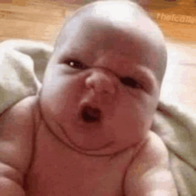 a baby is making a funny face while laying on a blanket on the floor .