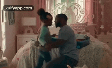 a man and a little girl are dancing on a bed in a pink bedroom .