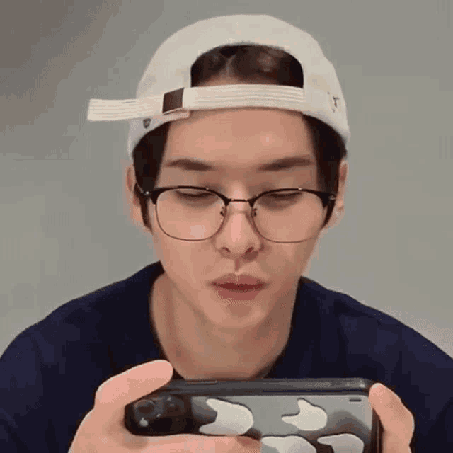 a man wearing glasses and a hat is holding a cell phone in his hand .