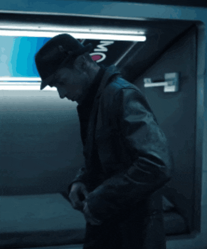 a man wearing a hat and a leather jacket stands in front of a sign that says mc on it