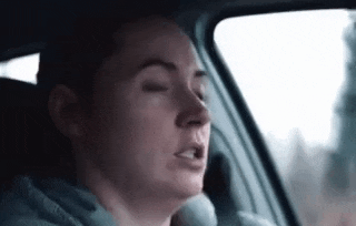 a woman is sitting in the driver 's seat of a car with her eyes closed and her mouth open .