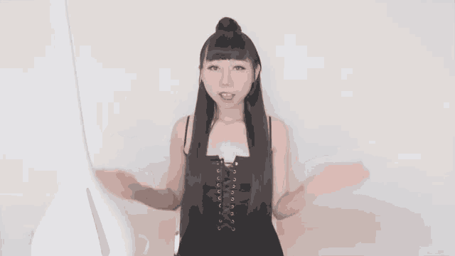 a woman with long black hair is sitting in front of a white vase and talking to the camera .