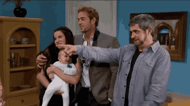 a woman holds a baby while two men point at it