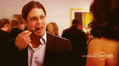a man in a suit is eating something from a spoon while a woman watches