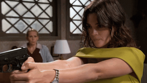 a woman in a yellow top is holding a gun in front of a window