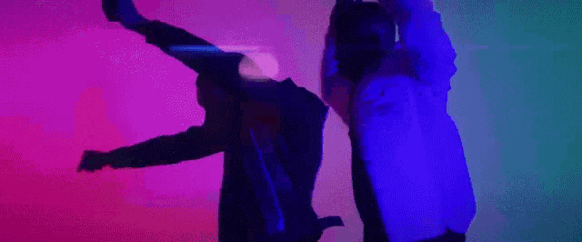 a man and a woman are dancing in a dark room with a purple and blue light behind them .