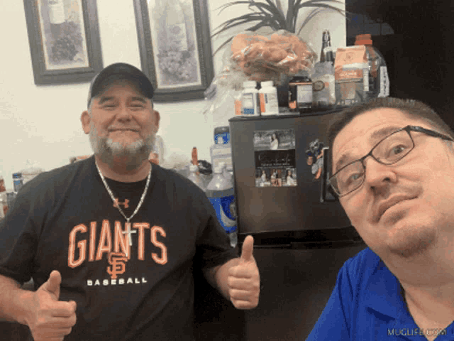 two men are posing for a picture and one has a giants baseball shirt on