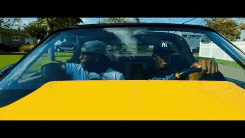 a man wearing a ny baseball cap is driving a yellow car