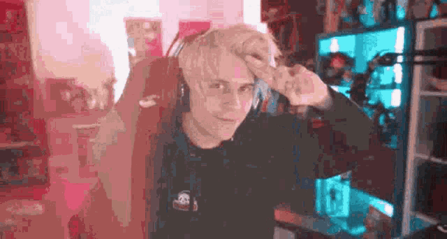 a man with blonde hair is wearing headphones and giving a peace sign while sitting in a gaming chair .
