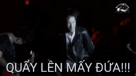 a man in a leather jacket is standing in front of a sign that says quay len may dua