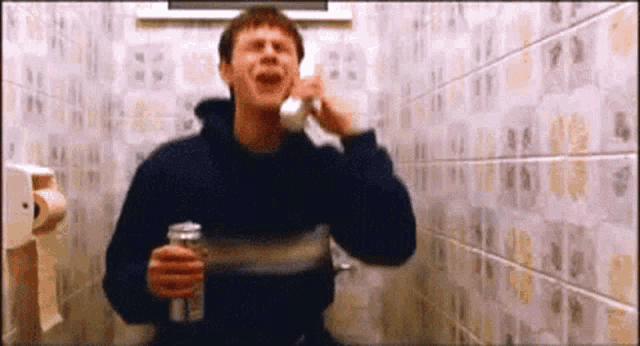 a man is talking on a phone in a bathroom while holding a can of beer