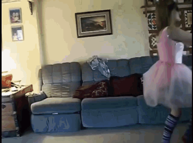 a girl in a pink dress is dancing in front of a couch