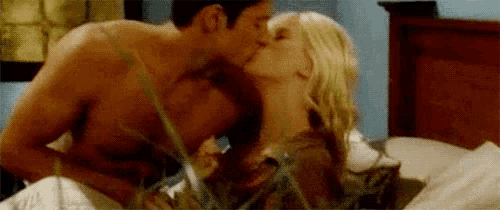 a man and a woman are kissing in bed . the man is shirtless and the woman is blonde .