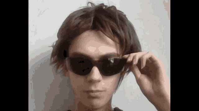a young man wearing sunglasses and a wig looks at the camera
