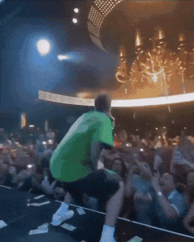 a man in a green shirt stands on a stage in front of a crowd of people