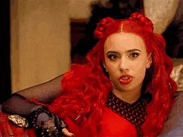 a woman with red hair and black gloves is sitting on a couch .