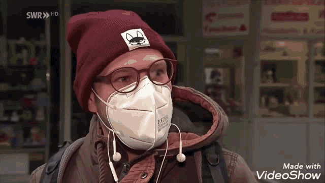 a man wearing a mask and a beanie with a cat on it is on a video show