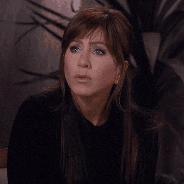 a woman with long brown hair and blue eyes is wearing a black sweater and making a funny face .