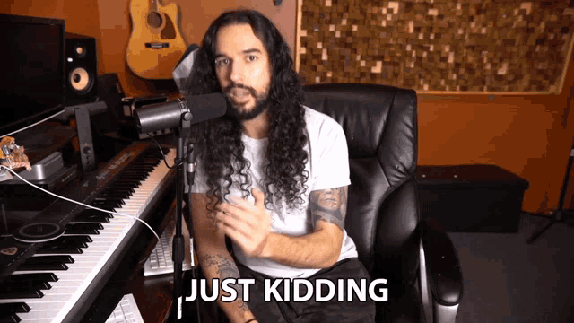 a man with long hair and a beard is sitting in front of a microphone with the words just kidding written below him