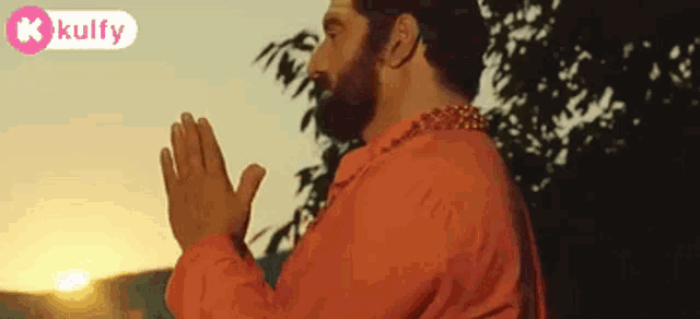 a man with a beard is praying with his hands folded in front of a tree .