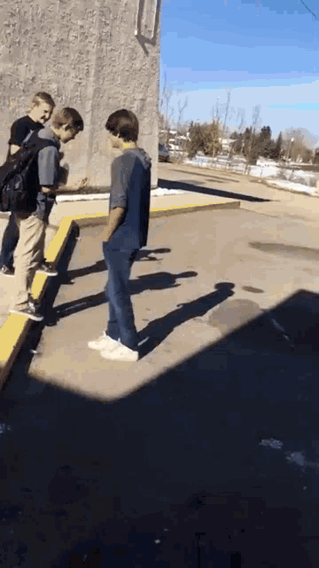 a group of boys are standing on a sidewalk looking at something