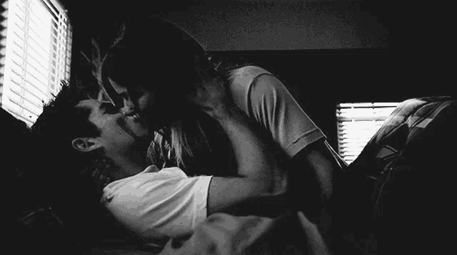 a man and a woman are kissing on a bed in front of a window .